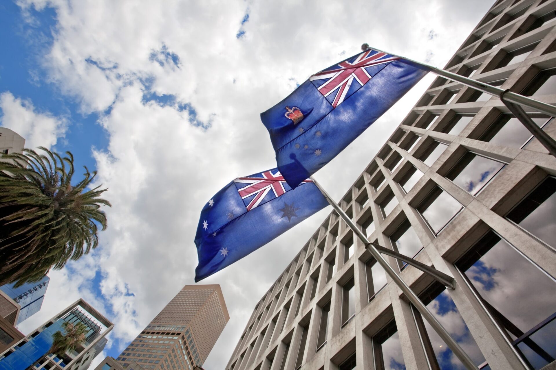 Low angle shot of Australian flags waving from a Government Building against a cloudy sky